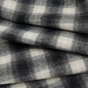 May include: Close-up of a folded fabric with a classic black and white checkered pattern. The fabric has a soft, textured appearance, with the light and dark squares creating a visually appealing design. The folds add depth and dimension to the textile.