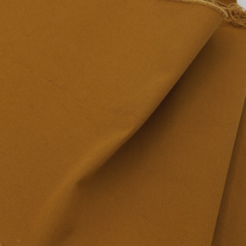 May include: Close-up of a brown fabric with a subtle texture. The fabric is folded and has a raw edge.