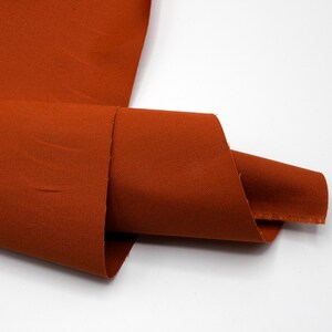May include: A close-up of a rust-colored fabric with a subtle texture. The fabric is folded in half and the edges are visible.