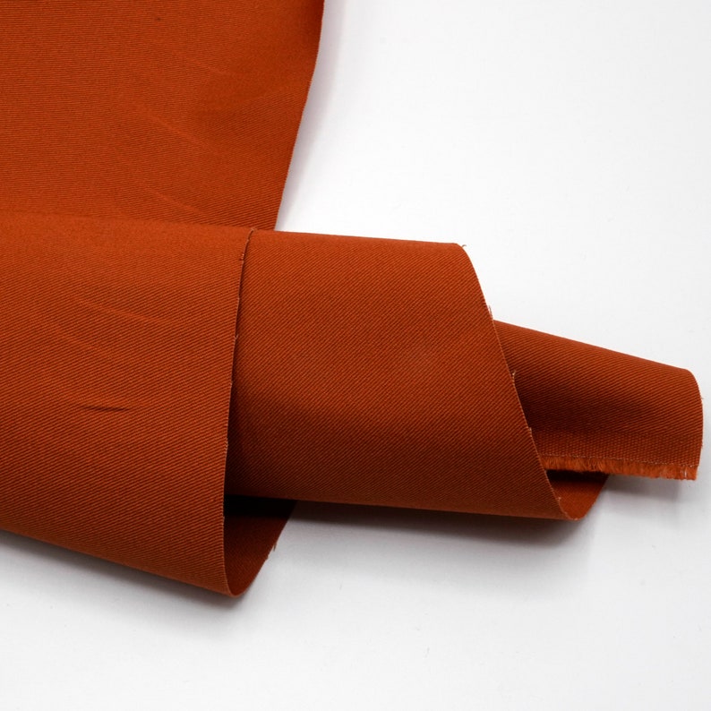 May include: A close-up of a rust-colored fabric with a subtle texture. The fabric is folded in half and the edges are visible.