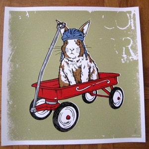 May include: A red wagon with a white and brown rabbit wearing a blue helmet. The wagon has a red handle and black wheels. The background is a green and white distressed pattern.