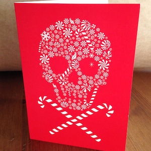 May include: A red card with a white skull and crossbones design. The skull is made up of white candy canes and peppermint swirls.