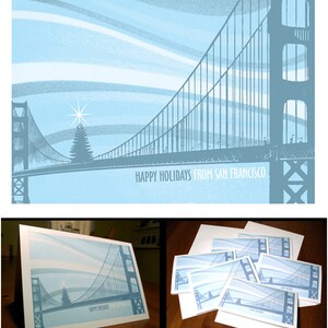 May include: A set of 16 holiday cards featuring a blue and white illustration of the Golden Gate Bridge with a Christmas tree in the foreground. The text "Happy Holidays from San Francisco" is printed on the cards. The cards are available for $16.  "16 Cards for $16 Bucks - store.gigart.com"