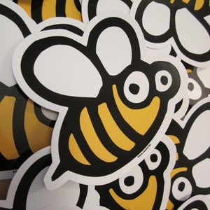 May include: A close-up of a pile of black and yellow bee stickers. The bees have white wings and large, round eyes.