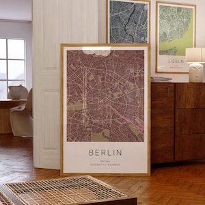 May include: A framed map print of Berlin, Germany, in shades of burgundy and tan. The city map is detailed with streets and parks. The print includes the city name and coordinates. Two other framed city maps are visible in the background.