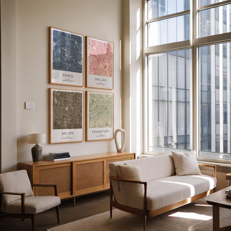 May include: Four framed city map prints hang on a wall. The maps are of Paris, Dallas, Milan, and Frankfurt. The prints have a neutral color palette with a wooden frame. The room also features a wooden cabinet, a sofa, and a chair.