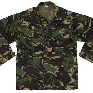 Peut inclure: Une chemise à manches longues boutonnée avec un motif camouflage forestier dans des tons vert foncé, marron et noir. La chemise comprend deux poches de poitrine à rabat boutonné, un col classique et un petit écusson drapeau sur la manche gauche.