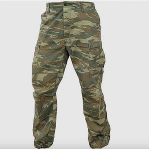 May include: Cargo trousers featuring a tiger stripe camouflage pattern in shades of olive green, brown, and tan. These trousers include a button fly closure, two side cargo pockets with flaps, and two front pockets, designed with a straight leg fit.