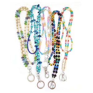 May include: A selection of beaded lanyards in diverse colours, such as blue, green, pink, and black. Each lanyard showcases a unique bead design and a silver clasp for attaching keys or an ID badge. The lanyards are presented against a white backdrop.
