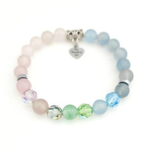 K&ouml;nnte beinhalten: Ein elastisches Armband mit verschiedenen runden Perlen in Rosa-, Blau- und Gr&uuml;nt&ouml;nen. Das Design umfasst matte und facettierte Kristallperlen, silberfarbene Zwischenelemente und einen herzf&ouml;rmigen Anh&auml;nger mit der Gravur My Beading Art.