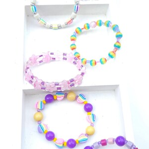May include: A collection of six colorful beaded bracelets featuring various shapes and patterns. The bracelets include round, star-shaped, and heart-shaped beads in shades of pink, purple, yellow, blue, green, and orange, arranged in diverse sequences.
