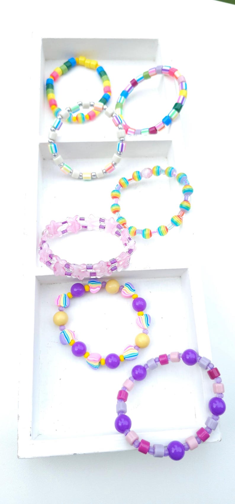 May include: A collection of six colorful beaded bracelets featuring various shapes and patterns. The bracelets include round, star-shaped, and heart-shaped beads in shades of pink, purple, yellow, blue, green, and orange, arranged in diverse sequences.