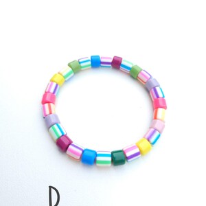 May include: A circular bracelet composed of small, cylindrical beads in a variety of bright colors including pink, blue, yellow, green, purple, and white. The beads feature horizontal striped patterns and solid colors. The letter D is visible.