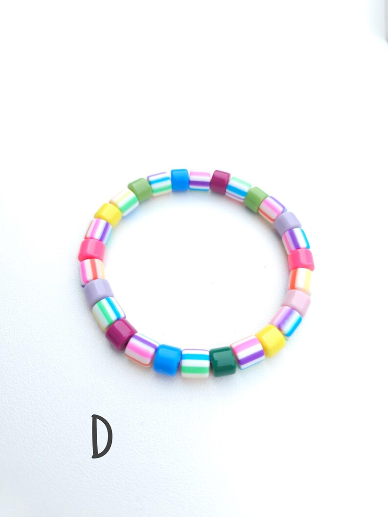 May include: A circular bracelet composed of small, cylindrical beads in a variety of bright colors including pink, blue, yellow, green, purple, and white. The beads feature horizontal striped patterns and solid colors. The letter D is visible.
