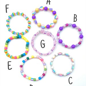 May include: Seven colorful beaded bracelets labeled A through G. Bracelet A has purple and heart beads. B features purple and pink spheres. C has white and striped beads. D uses multicolored cubes. E has bright cubes. F has rainbow beads. G is pink.