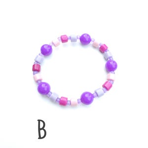 May include: A circular bracelet featuring a repeating pattern of purple spherical beads, light purple cylindrical beads, pink square beads, and light pink cylindrical beads strung together. The letter B is printed in black below the bracelet.