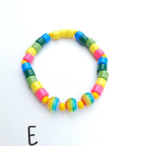 May include: A circular bracelet featuring a repeating pattern of cylindrical beads in yellow, pink, blue, and green, interspersed with small yellow spacer beads and three larger spherical beads with multicolored vertical stripes, marked with the letter E.