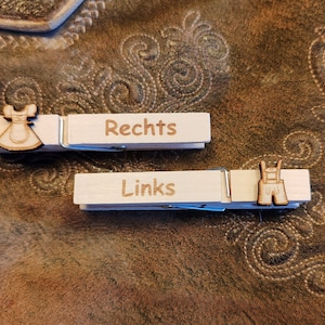 May include: Two wooden clothespins with the words "Rechts" and "Links" written on them. The clothespins are decorated with a small wooden cutout of a dirndl and lederhosen.