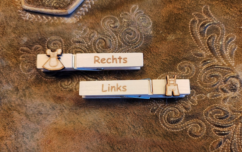 May include: Two wooden clothespins with the words "Rechts" and "Links" written on them. The clothespins are decorated with a small wooden cutout of a dirndl and lederhosen.