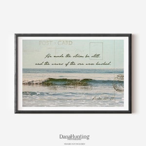 Horizontal photo of a calm glassy ocean wave.  Psalm 107:29 is imposed above the water in a handwriting script. Faint details of a vintage postcard create a collage effect.  Colors are pastel blue-green.