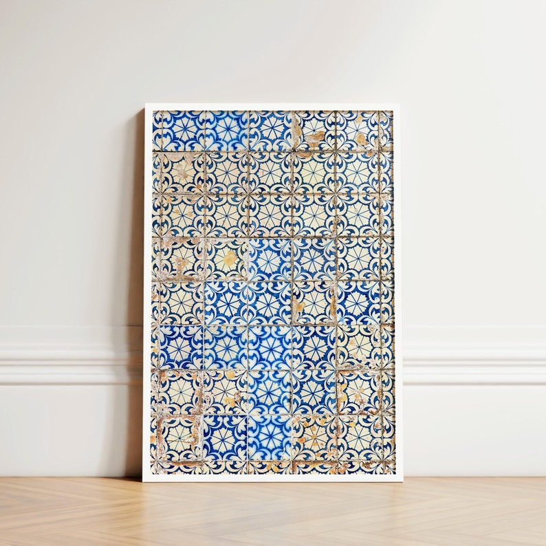 May include: A framed print featuring a pattern of blue and white tiles. The tiles have a floral design and are arranged in a grid. The print is leaning against a white wall on a wooden floor.