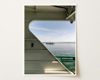 May include: A view from inside a ferry deck looking out through a large triangular window at a distant ferry on the water. The interior structure is off-white with a green metal railing visible in the lower right corner of the window frame.