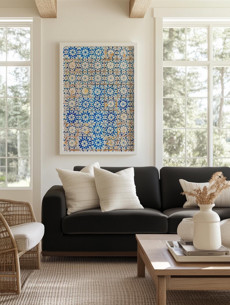 May include: A living room scene featuring a black sofa with cream-colored pillows, a wooden coffee table, and a framed artwork with a blue and white tile pattern. A woven chair and a beige rug complete the cozy interior.