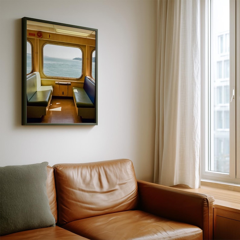 May include: A framed wall art print depicting the interior of a ferry or train cabin with yellow walls, a large window overlooking a body of water, and two rows of bench seating in blue and white, all enclosed in a thin black frame.