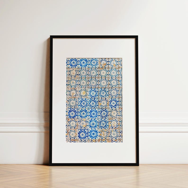 May include: Framed art print featuring a detailed pattern of blue and white tiles. The tiles have a floral design with yellow accents. The artwork is set in a black frame and rests on a wooden surface.
