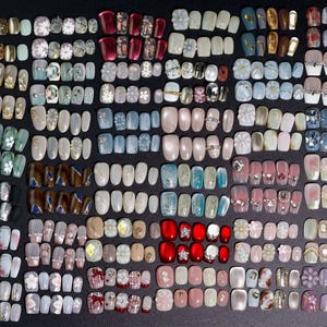 Puede incluir: Una colecci&oacute;n de m&aacute;s de 100 u&ntilde;as postizas coloridas, decorativas y con dise&ntilde;os. Las u&ntilde;as est&aacute;n dispuestas en filas y columnas, mostrando una variedad de dise&ntilde;os, incluyendo patrones florales, geom&eacute;tricos y abstractos.