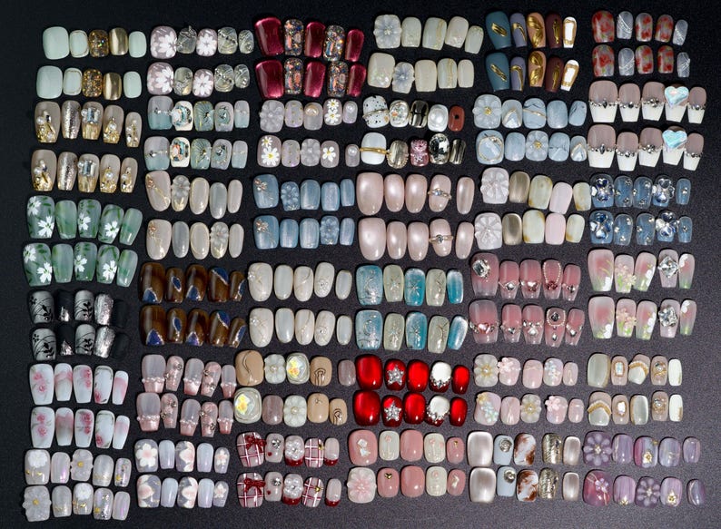 Puede incluir: Una colecci&oacute;n de m&aacute;s de 100 u&ntilde;as postizas coloridas, decorativas y con dise&ntilde;os. Las u&ntilde;as est&aacute;n dispuestas en filas y columnas, mostrando una variedad de dise&ntilde;os, incluyendo patrones florales, geom&eacute;tricos y abstractos.