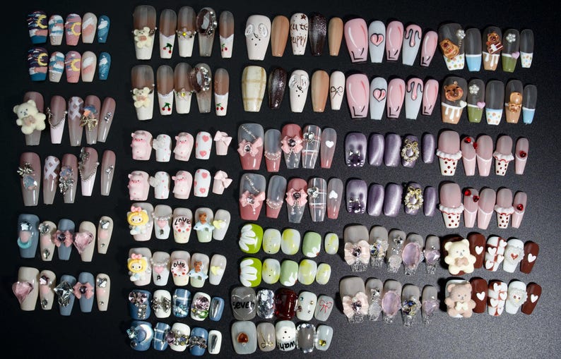 Puede incluir: Una colecci&oacute;n de 20 filas de u&ntilde;as postizas decorativas y coloridas. Cada fila presenta un dise&ntilde;o diferente, que incluye personajes de dibujos animados, corazones, flores y patrones geom&eacute;tricos.