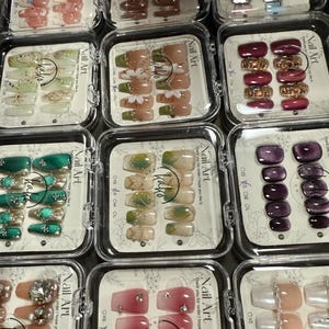 Puede incluir: Surtido de diez juegos de u&ntilde;as postizas con varios dise&ntilde;os y colores. Cada juego incluye diez u&ntilde;as con un dise&ntilde;o diferente. Los dise&ntilde;os incluyen flores, estrellas, pedrer&iacute;a y purpurina. Las u&ntilde;as est&aacute;n empaquetadas en cajas de pl&aacute;stico transparente con el nombre de la marca "kako" impreso en ellas.