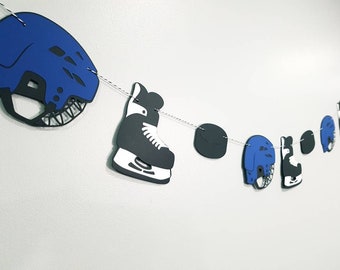 May include: A hockey-themed paper banner with blue and black hockey helmets, skates, and pucks. The banner is strung together with white twine.