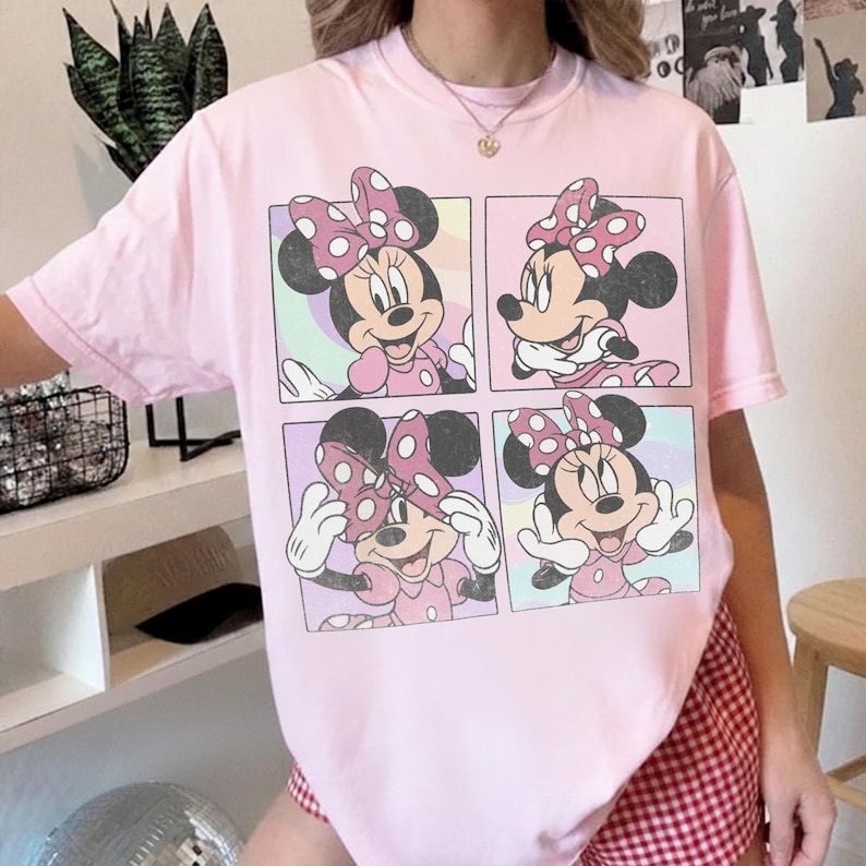 Puede incluir: Una camiseta de manga corta de color rosa claro con un gran estampado gr&aacute;fico rectangular dividido en cuatro paneles. Cada panel muestra una ilustraci&oacute;n diferente de Minnie Mouse con un lazo de lunares sobre fondos de tonos pastel.