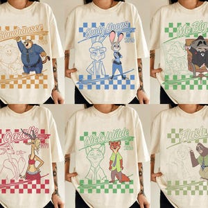 May include: A collection of six off-white t-shirts featuring Zootopia character graphics. Each shirt displays a character name, a year, a checkered border, and a colored illustration of Clawhauser, Judy Hopps, Mr. Big, Gazelle, Nick Wilde, or Flash.