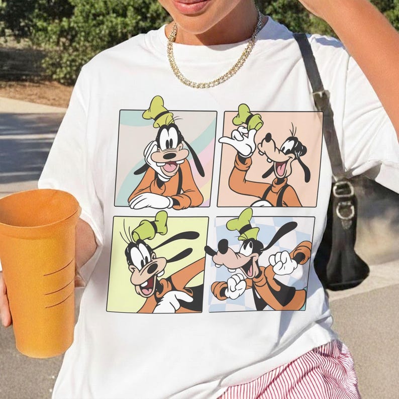 Puede incluir: Una camiseta blanca con un estampado gr&aacute;fico de cuatro paneles distintos, cada uno mostrando al personaje de dibujos animados Goofy en diferentes poses, vistiendo un su&eacute;ter naranja, chaleco negro y un sombrero verde sobre fondos pastel.