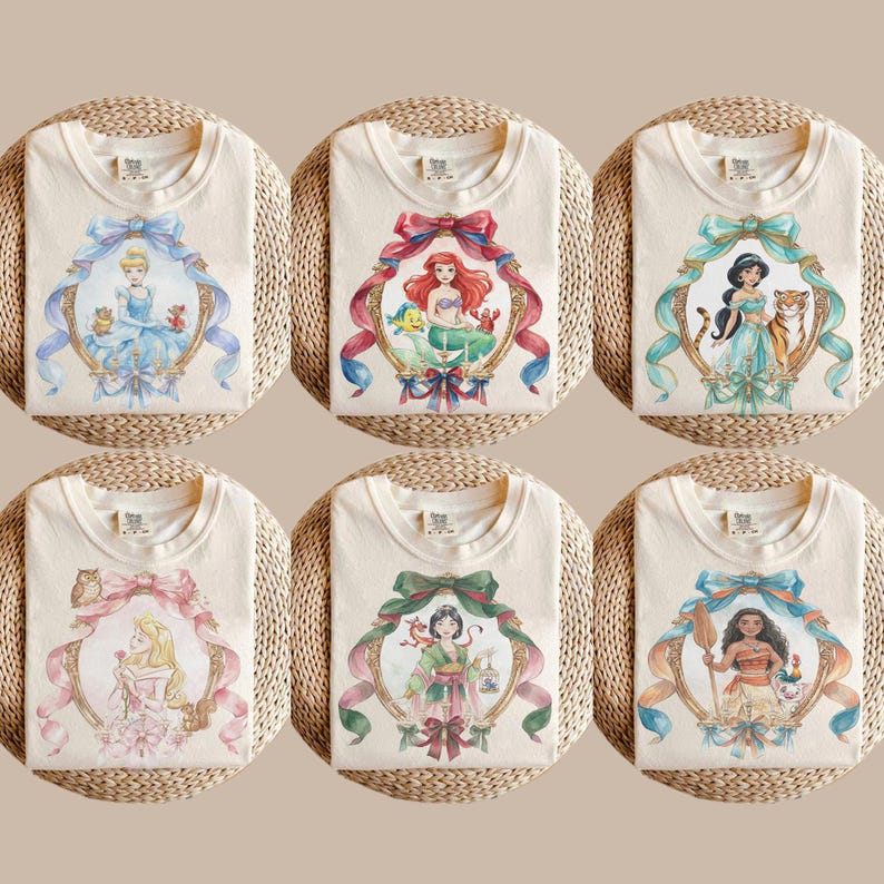 May include: Six cream-colored t-shirts with watercolor illustrations of Disney princesses. Each shirt features a different princess within a decorative gold frame with a ribbon. The princesses include Cinderella, Ariel, Jasmine, Aurora, Mulan, and Moana.