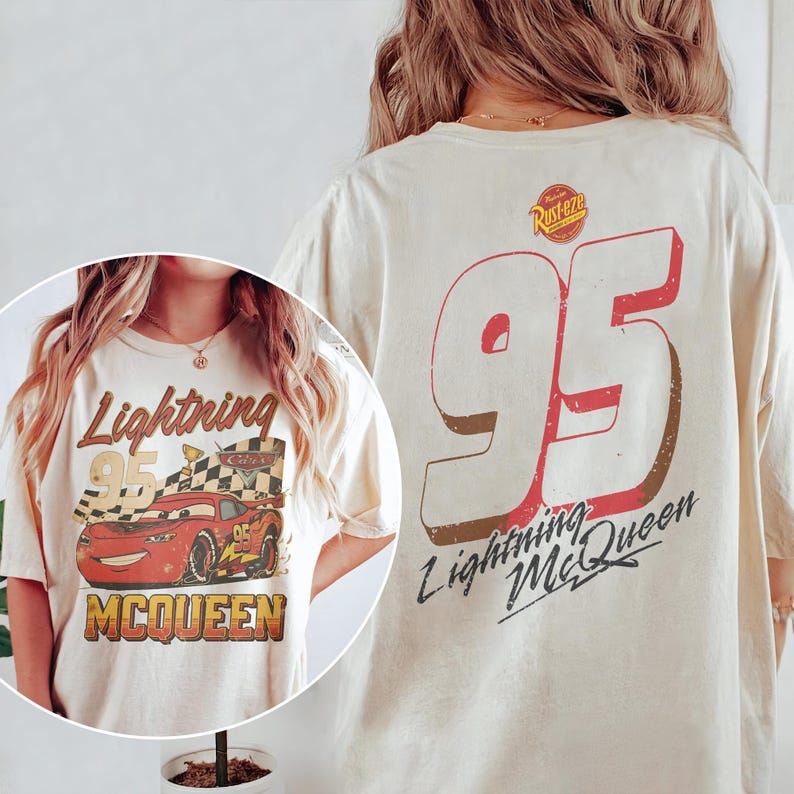 May include: Cream-colored t-shirt featuring a graphic of Lightning McQueen from the movie Cars. The front design includes the text "Lightning 95 McQueen" with an image of the race car. The back of the shirt displays a large "95" and "Lightning McQueen" text.