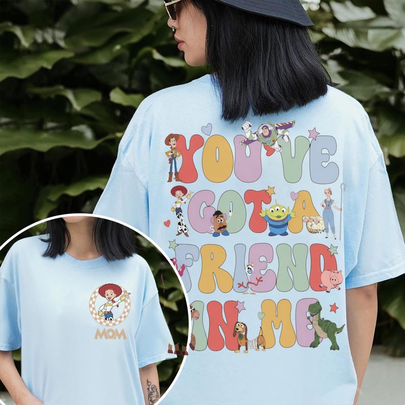 Peut inclure: Un t-shirt bleu clair avec un grand motif au dos portant le texte "YOU'VE GOT A FRIEND IN ME" en lettres ondul&eacute;es color&eacute;es entour&eacute;es de personnages de Toy Story. La poitrine affiche un graphique circulaire de Jessie et le mot "MOM".