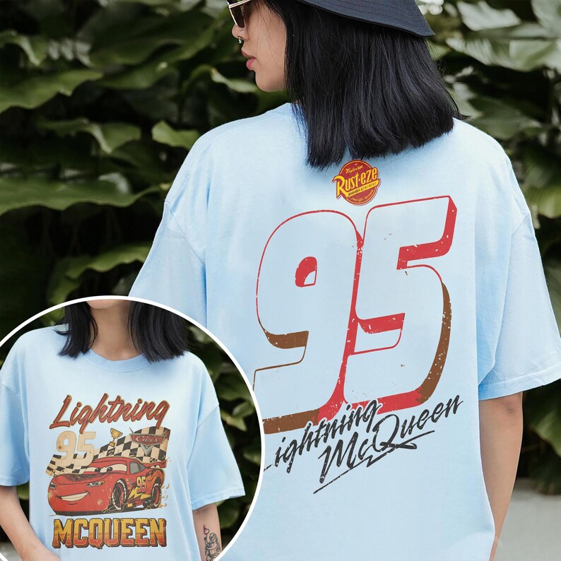 May include: Light blue t-shirt featuring a large "95" graphic in red and brown, with "Lightning McQueen" text. The shirt also has a smaller graphic on the front with the text "Lightning 95 McQueen".