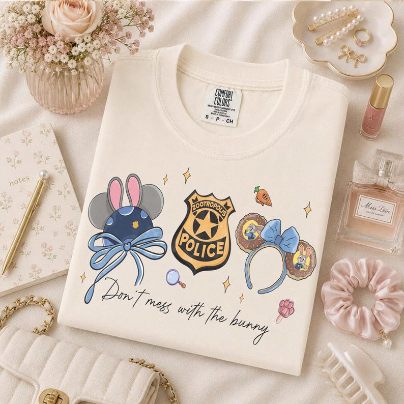 May include: A cream-colored crewneck t-shirt featuring a graphic print of Zootropolis-themed mouse ears, a police badge, and a carrot. The text "Don't mess with the bunny" is printed in black script below the illustrations on the front of the shirt.