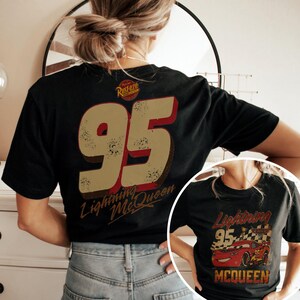 May include: Black t-shirt featuring a distressed design with the number "95" in tan and red, and the words "Lightning McQueen." A smaller image of Lightning McQueen is also visible. The shirt has a vintage, worn look.