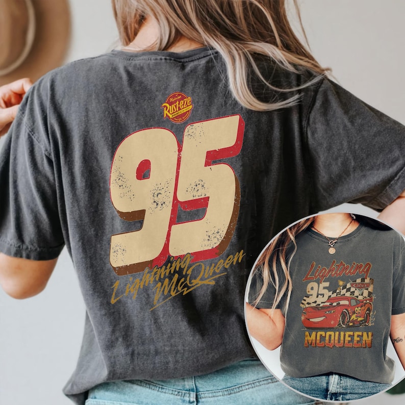 May include: Dark gray t-shirt featuring a distressed design of Lightning McQueen's number 95. The shirt includes the text "Lightning McQueen" and the Rust-eze logo. A smaller image of the design is visible on the lower right.