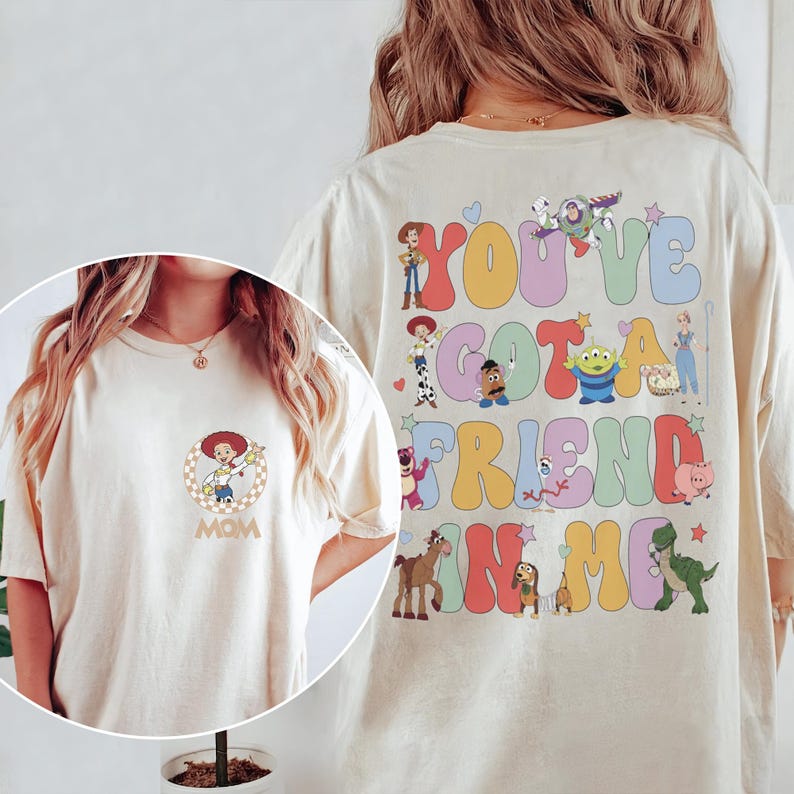 Peut inclure: Un t-shirt couleur cr&egrave;me avec un petit motif circulaire de Jessie sur la poitrine et le mot MOM en dessous. Le dos pr&eacute;sente de grandes lettres color&eacute;es de style bulle formant YOU'VE GOT A FRIEND IN ME, entour&eacute;es de divers personnages Toy Story.