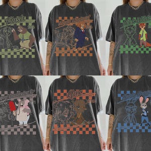 May include: A charcoal gray t-shirt featuring six distinct graphic designs of animated characters including Flash, Mayor Lionheart, Nick Wilde, Jerry Jumbeaux Jr, Yax, and Judy Hopps. Each design includes a checkered background and the character name.