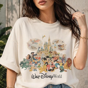 Puede incluir: Camiseta color crema con un gr&aacute;fico colorido de personajes de Disney, incluyendo Mickey Mouse, el Pato Donald y el castillo de Cenicienta. Las palabras "Walt Disney World" est&aacute;n impresas en negro debajo de los personajes.