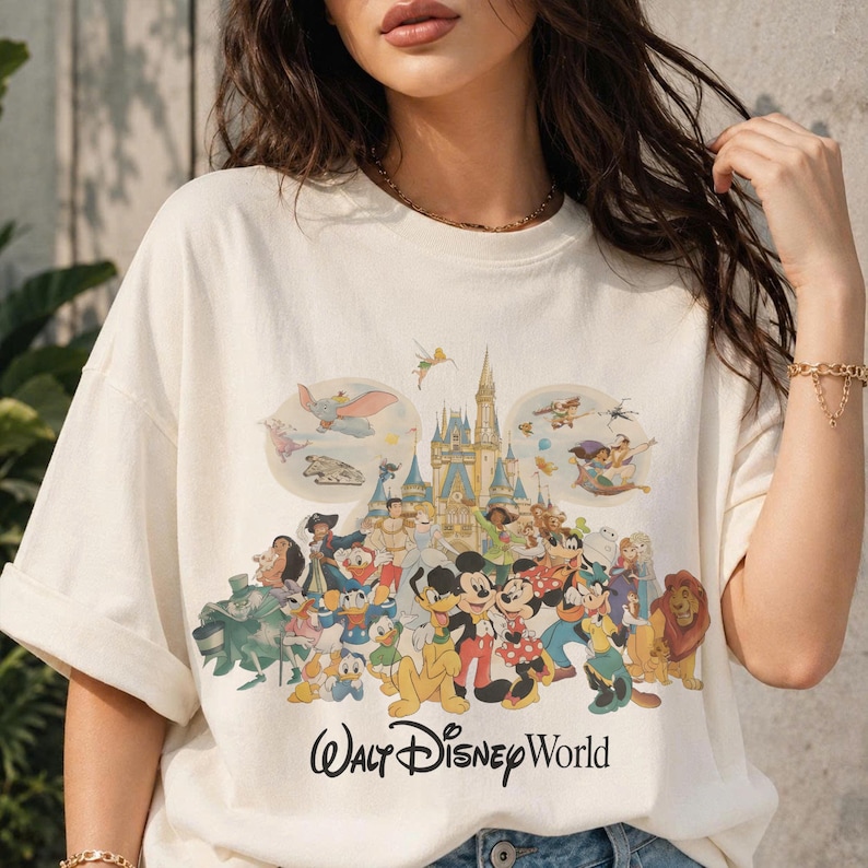 Puede incluir: Camiseta color crema con un gr&aacute;fico colorido de personajes de Disney, incluyendo Mickey Mouse, el Pato Donald y el castillo de Cenicienta. Las palabras "Walt Disney World" est&aacute;n impresas en negro debajo de los personajes.