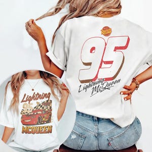 May include: White t-shirt featuring a graphic of Lightning McQueen from the movie Cars. The design includes the number 95, the words "Lightning McQueen", and the Rust-eze logo. The shirt is a casual, comfortable style.