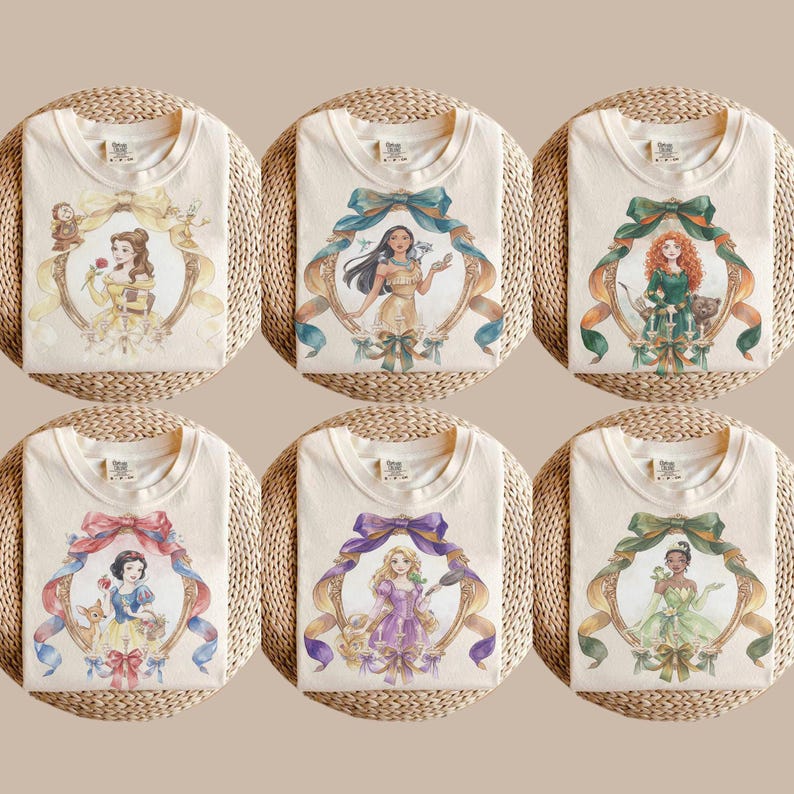 May include: Six cream-colored t-shirts featuring watercolor illustrations of Disney princesses. Each shirt displays a different princess within a decorative frame with ribbons and bows. The princesses include Belle, Pocahontas, Merida, Snow White, Rapunzel, and Tiana.